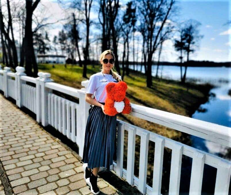 A woman holding a rose bear while walking near a lake